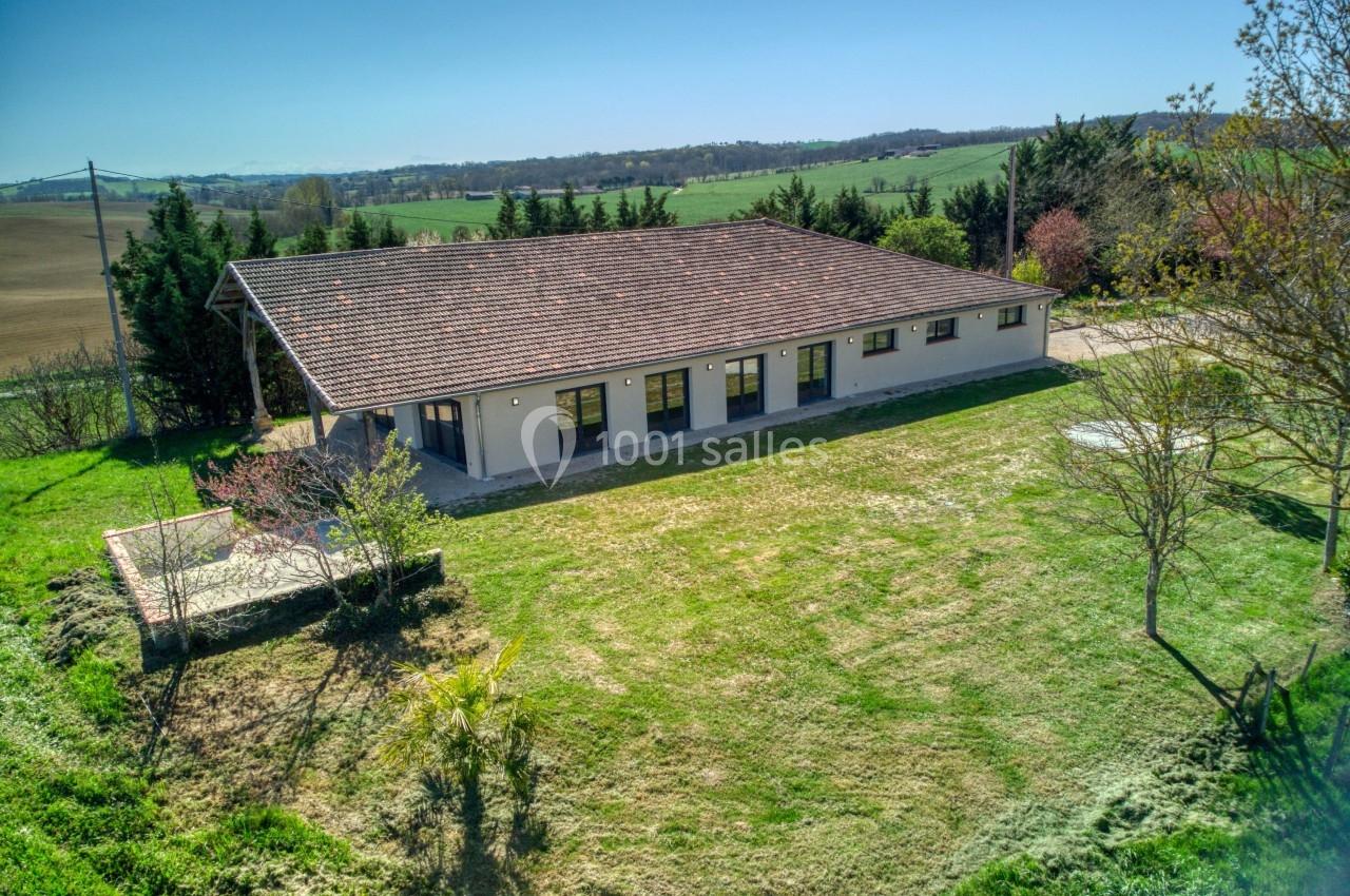 Bâtiment rectangulaire avec toit en tuiles, entouré de pelouse et d'arbres, dans un paysage rural.
