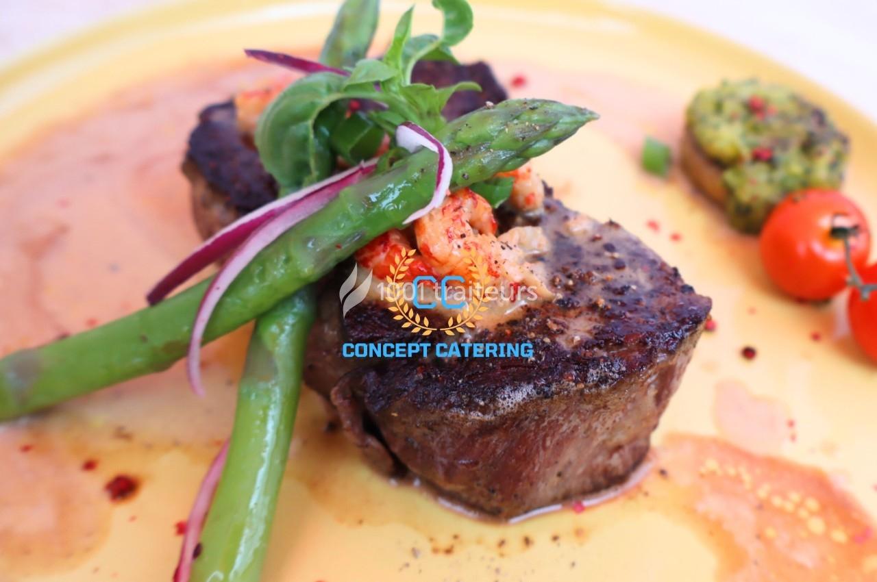 Pièce de viande grillée garnie d'asperges, écrevisses et légumes, servie sur une assiette jaune.