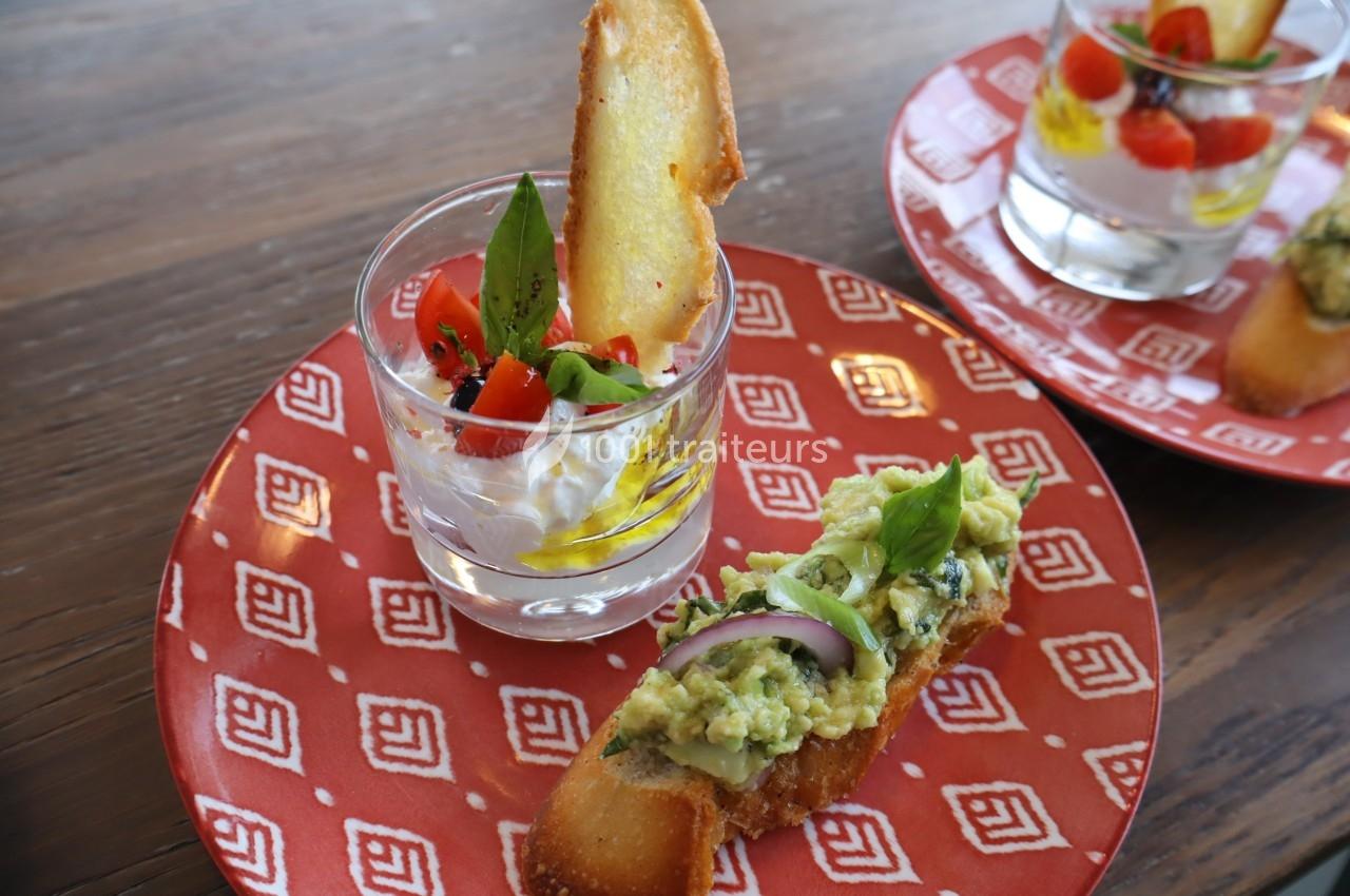 Un verre de burrata avec tomates cerises et basilic, accompagné d'une tartine à l'avocat sur une assiette rouge.