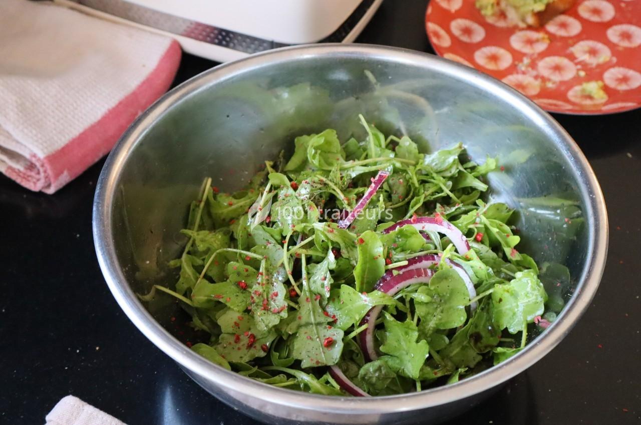 Salade de roquette fraîche avec rondelles d'oignon rouge et épices dans un saladier en métal sur un plan de travail.