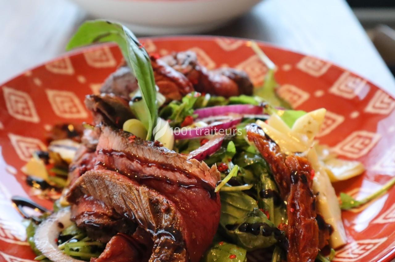 Assiette de salade garnie de tranches de viande, champignons grillés, oignons rouges et sauce balsamique.
