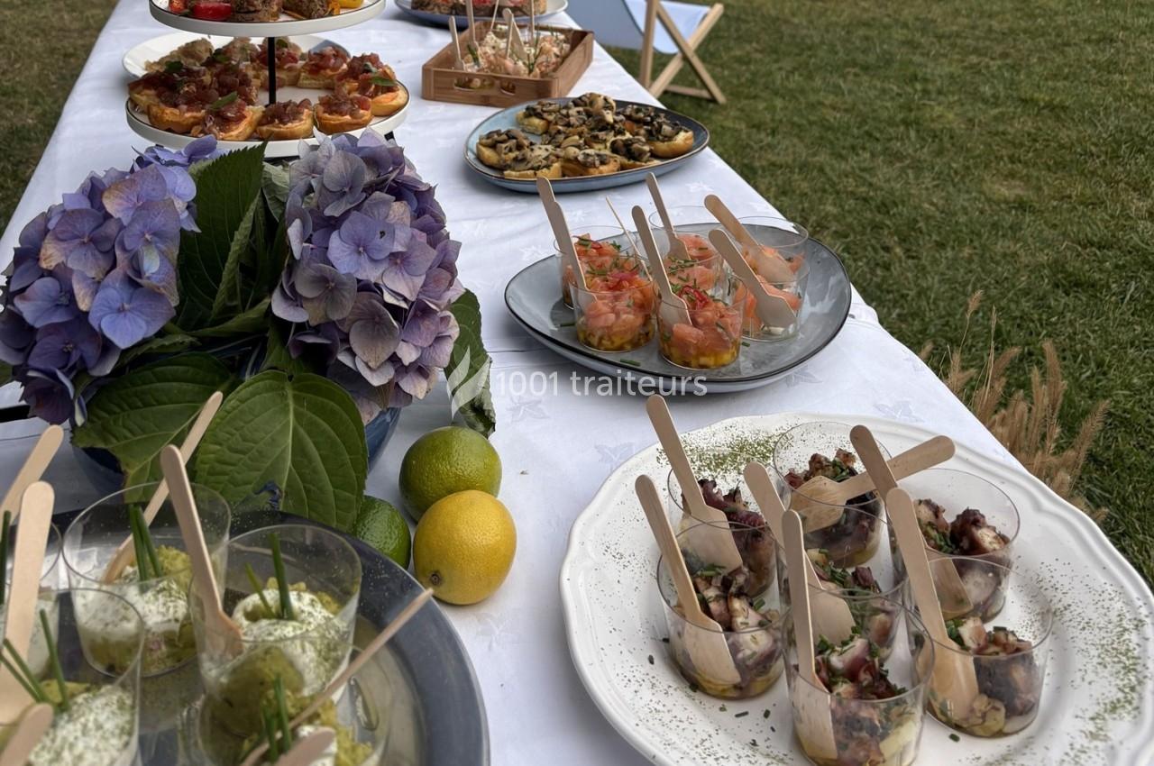 Buffet en plein air avec divers plats et verrines sur une table blanche, décorée d'hortensias et de citrons.