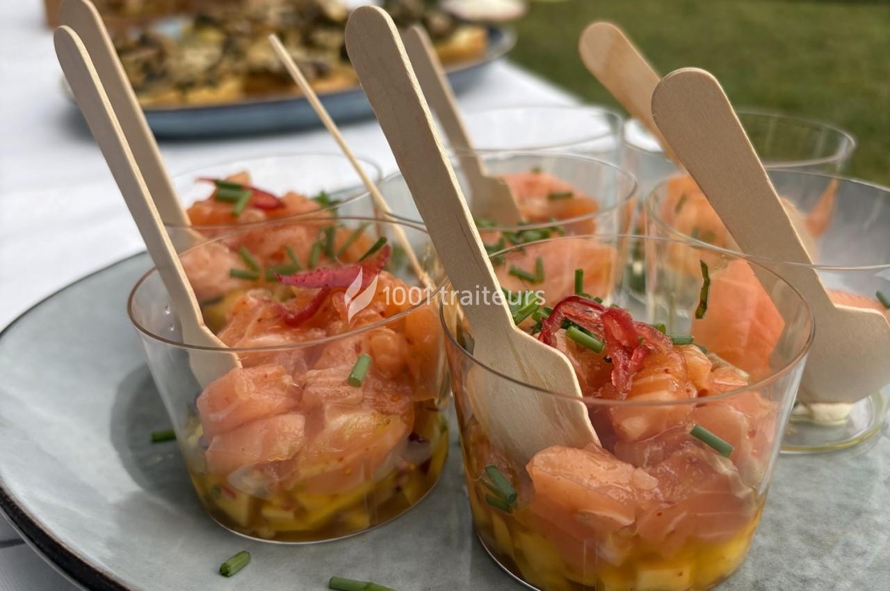 Verrines de tartare de saumon avec mangue, ciboulette et piments, servies avec des cuillères en bois sur une assiette.