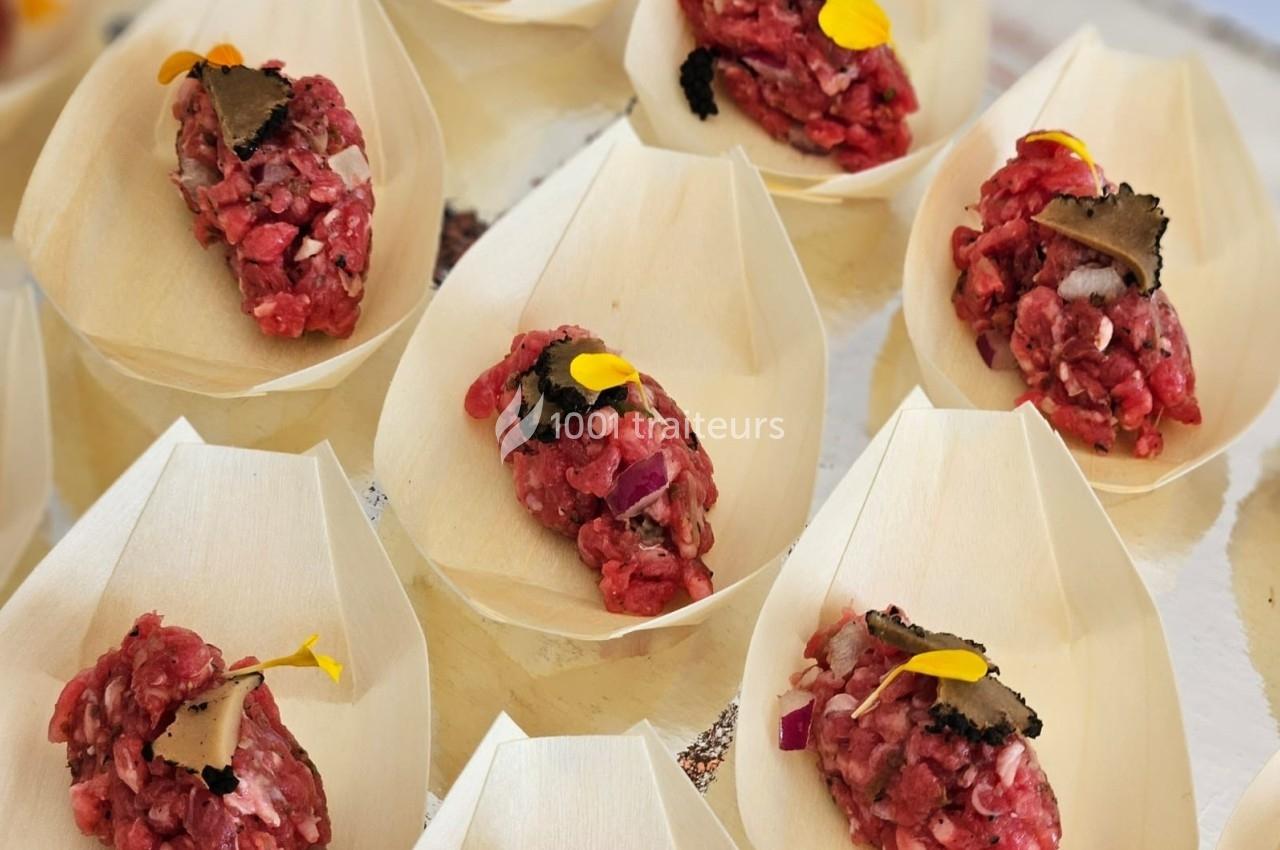 Portions de tartare de bœuf garnies de truffes et de fleurs comestibles, présentées dans des coupelles en bois.