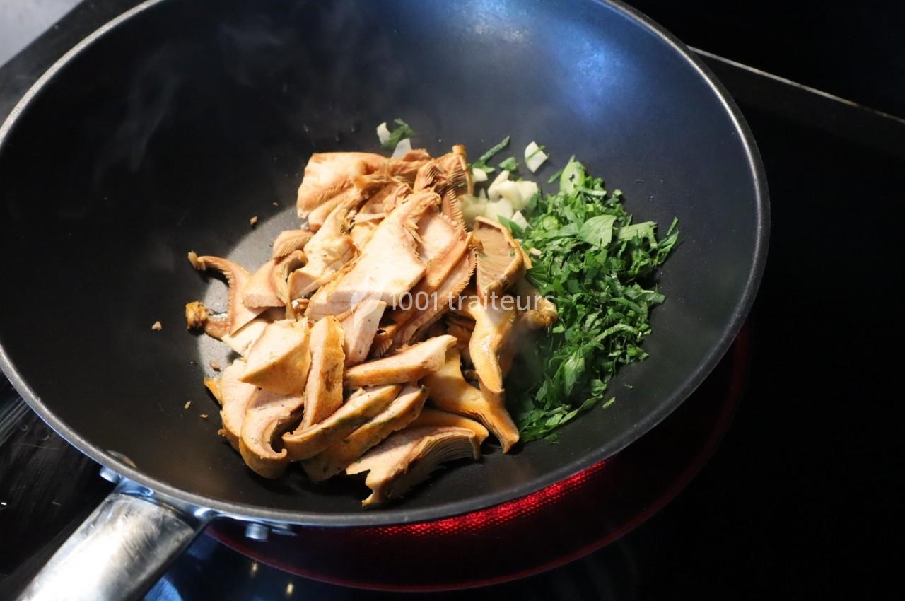 Champignons, ail émincé et herbes fraîches cuisant dans une poêle noire sur une plaque chauffante.