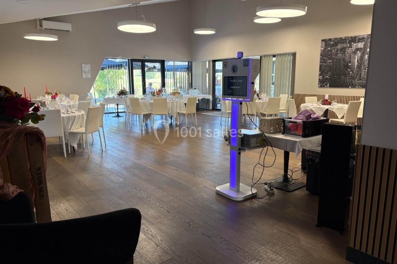 Salle de réception lumineuse avec tables dressées, décorations élégantes et borne photo interactive au premier plan.