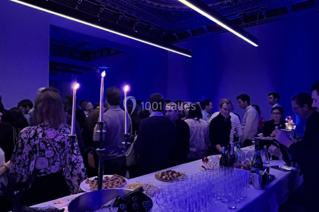 Groupe de personnes rassemblées dans une salle sombre éclairée par des lumières bleues, avec un buffet au premier plan.