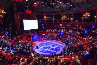 Salle vide avec éclairage rouge, rideaux en arrière-plan, scène surélevée et comptoirs alignés sur les côtés.