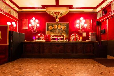 Salle vide avec éclairage rouge, rideaux en arrière-plan, scène surélevée et comptoirs alignés sur les côtés.