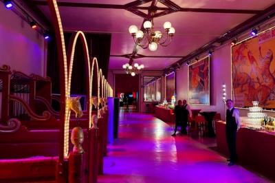 Salle vide avec éclairage rouge, rideaux en arrière-plan, scène surélevée et comptoirs alignés sur les côtés.