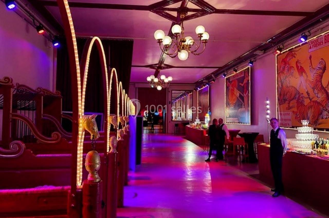 Salle décorée avec des lumières colorées, affiches rétro sur les murs et espace aménagé pour un événement.