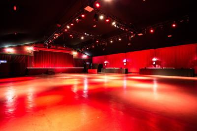 Salle vide avec éclairage rouge, rideaux en arrière-plan, scène surélevée et comptoirs alignés sur les côtés.
