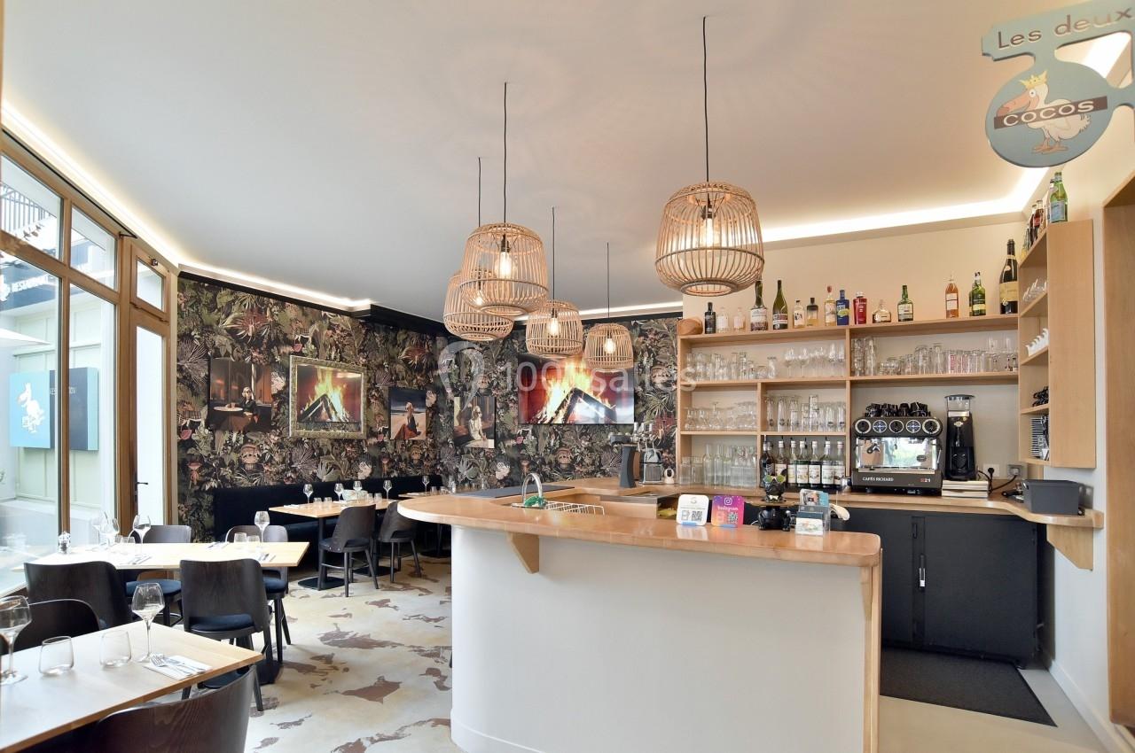Intérieur d'un restaurant avec un bar en bois, des luminaires suspendus et une décoration murale florale.