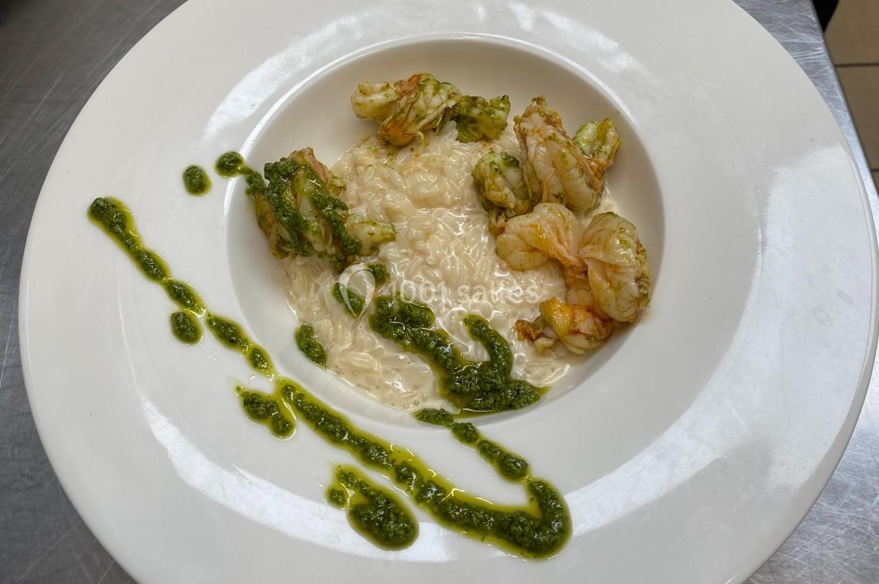 Assiette de risotto crémeux accompagné de crevettes et décorée de sauce verte.