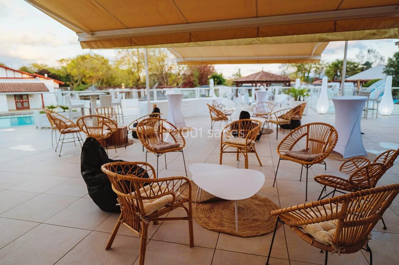 Terrasse aménagée avec des fauteuils en rotin, une table basse blanche et des parasols, près d'une piscine extérieure.