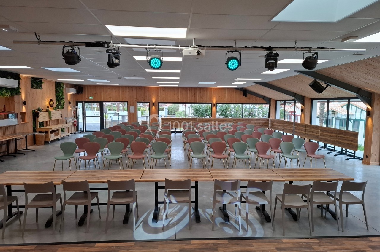 Salle de conférence lumineuse avec des rangées de chaises alignées face à une table et un espace scénique.