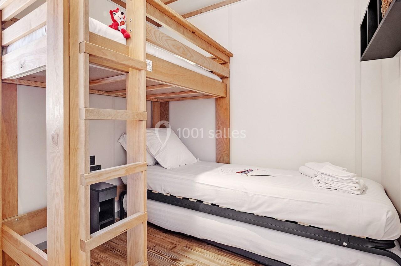 Lit superposé en bois clair avec un lit simple en dessous, dans une chambre minimaliste au sol en bois.