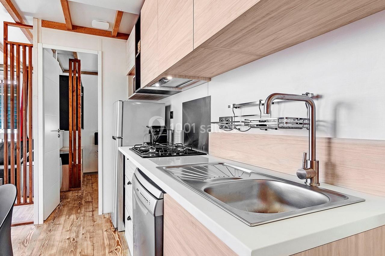 Cuisine compacte moderne avec plan de travail clair, évier en inox, plaques de cuisson et rangements en bois clair.