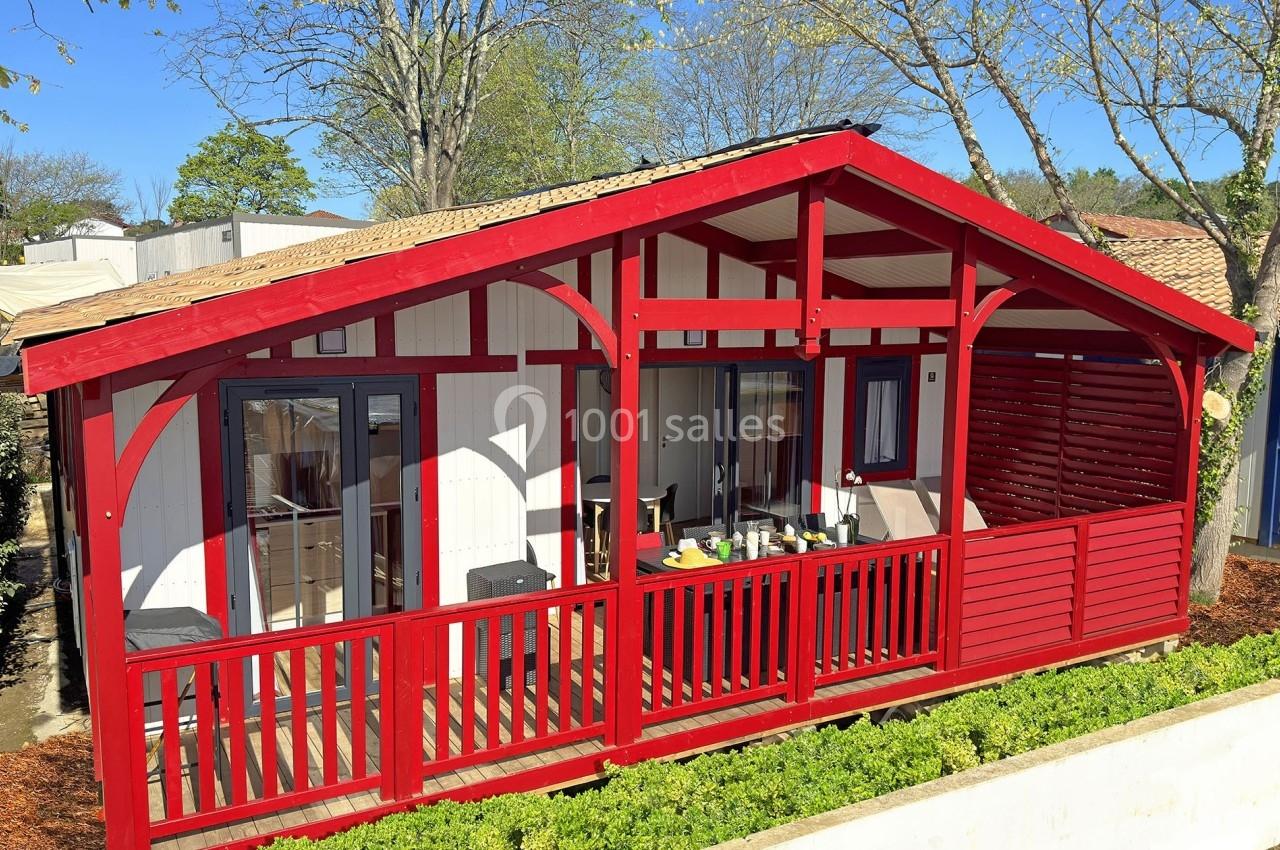 Chalet en bois rouge avec terrasse couverte, entouré de verdure et situé dans un environnement arboré.