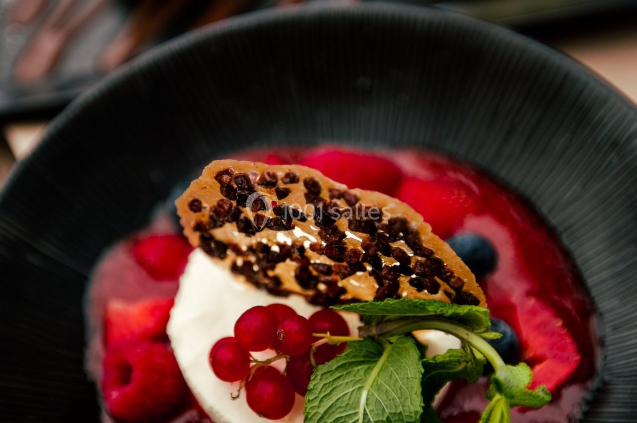 Dessert composé de fruits rouges, crème fouettée, tuile croustillante et coulis, présenté dans une assiette noire.