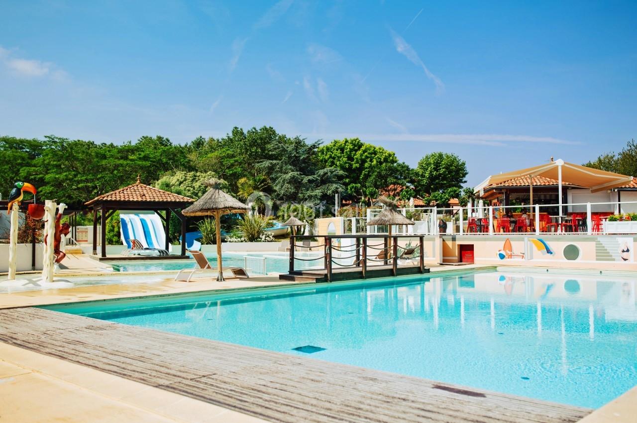 Piscine extérieure avec parasols en chaume, transats et terrasse ombragée dans un cadre verdoyant.