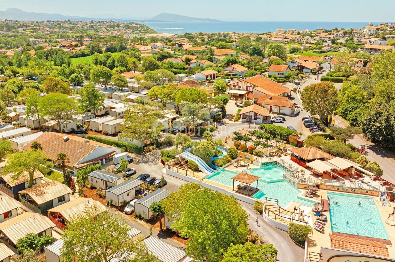 Vue aérienne d'un camping avec piscines, toboggans, mobil-homes et végétation, situé près de la côte et des montagnes.