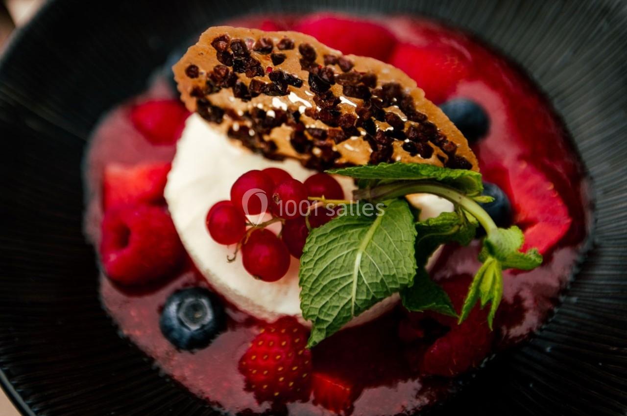 Dessert composé de fruits rouges, crème blanche, feuille de menthe et tuile croustillante sur une assiette noire.
