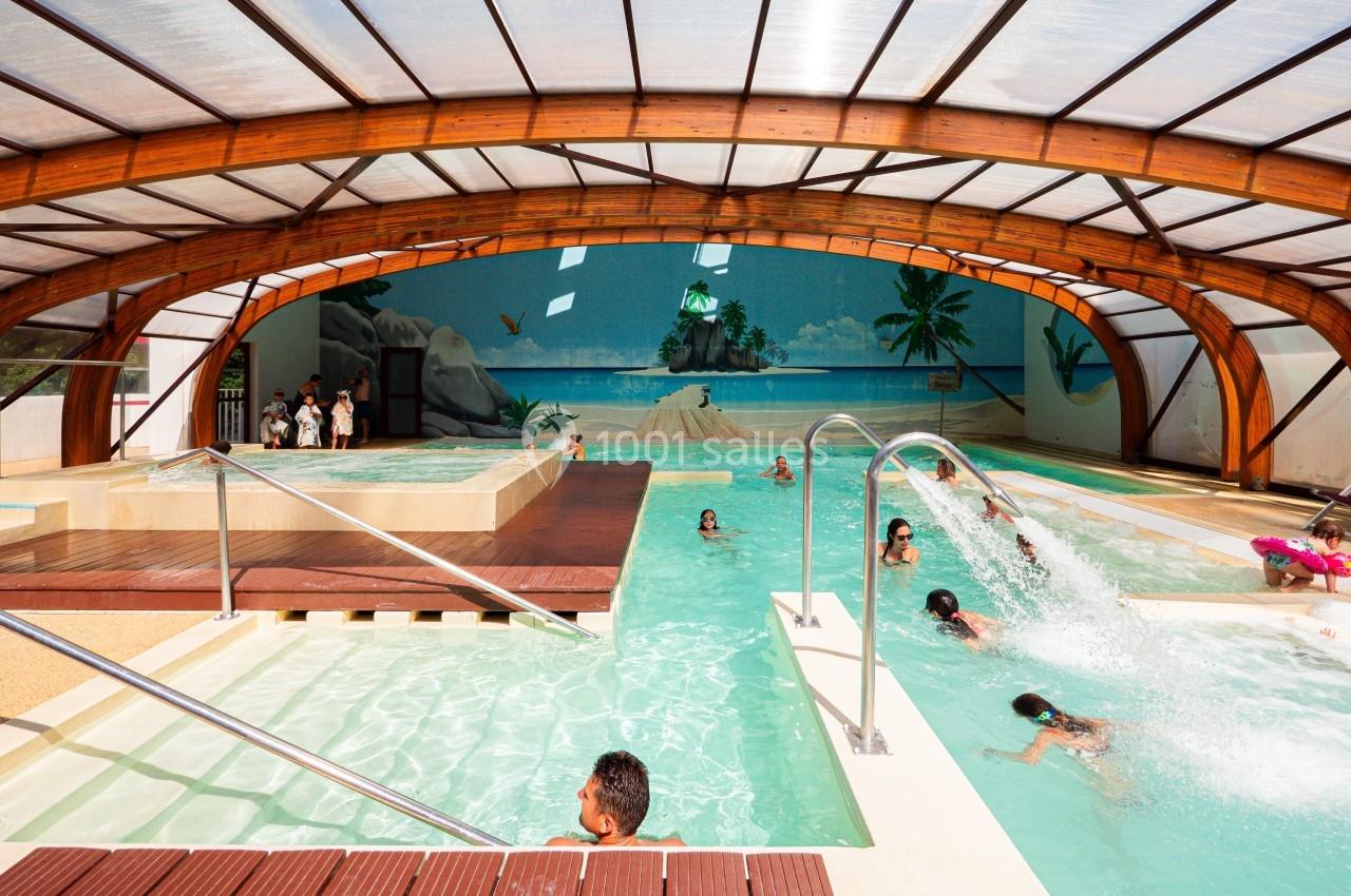 Piscine couverte avec jets d'eau, bassin pour enfants et décor mural tropical, fréquentée par plusieurs personnes.