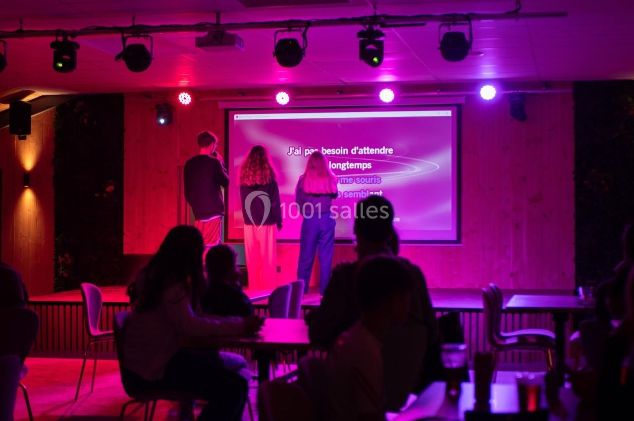 Des personnes chantent sur une scène de karaoké dans une salle éclairée par des lumières colorées.