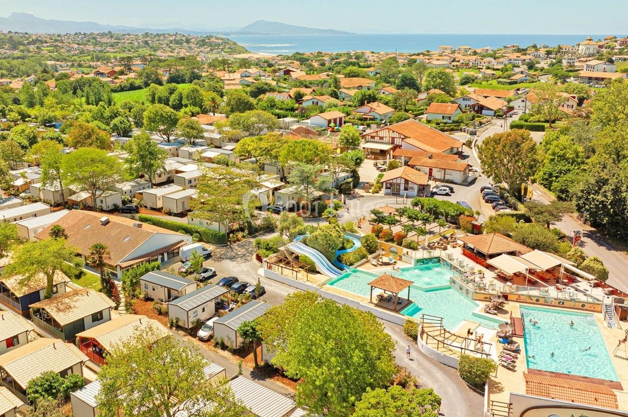 Vue aérienne d'un camping avec piscines, toboggan, mobil-homes et paysage côtier en arrière-plan.