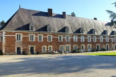 Cour pavée avec un bâtiment en briques rouges et toit en ardoise, entouré de végétation sous un ciel bleu.