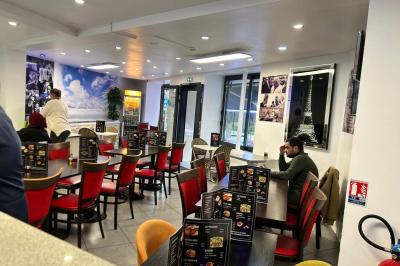 Salle de restaurant lumineuse avec tables et chaises rouges, un client assis et un employé au comptoir.