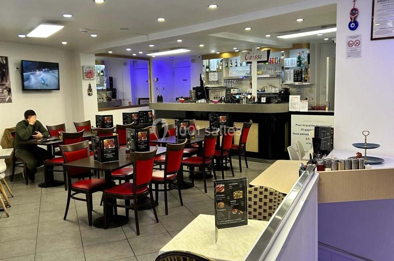 Salle de restaurant avec tables et chaises rouges, un comptoir en arrière-plan et un client assis seul.