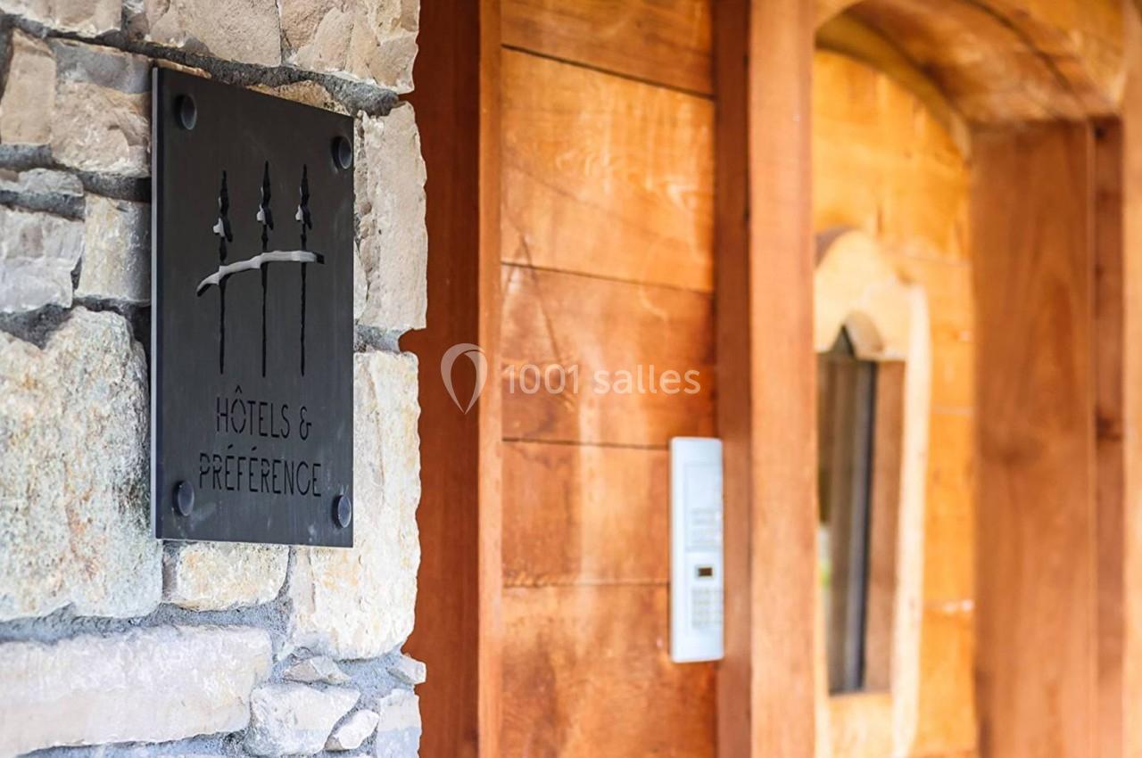 Plaque en métal avec un logo et l'inscription ’Hôtels & Préférence’, fixée sur un mur en pierre près d'une porte en bois.