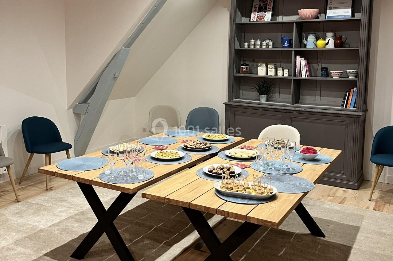Table en bois dressée avec des assiettes, des verres et des plats variés dans une salle à manger avec étagère en arrière…