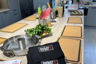 Deux femmes souriantes en tablier, l'une tenant une spatule rouge, l'autre un batteur électrique, dans une cuisine.