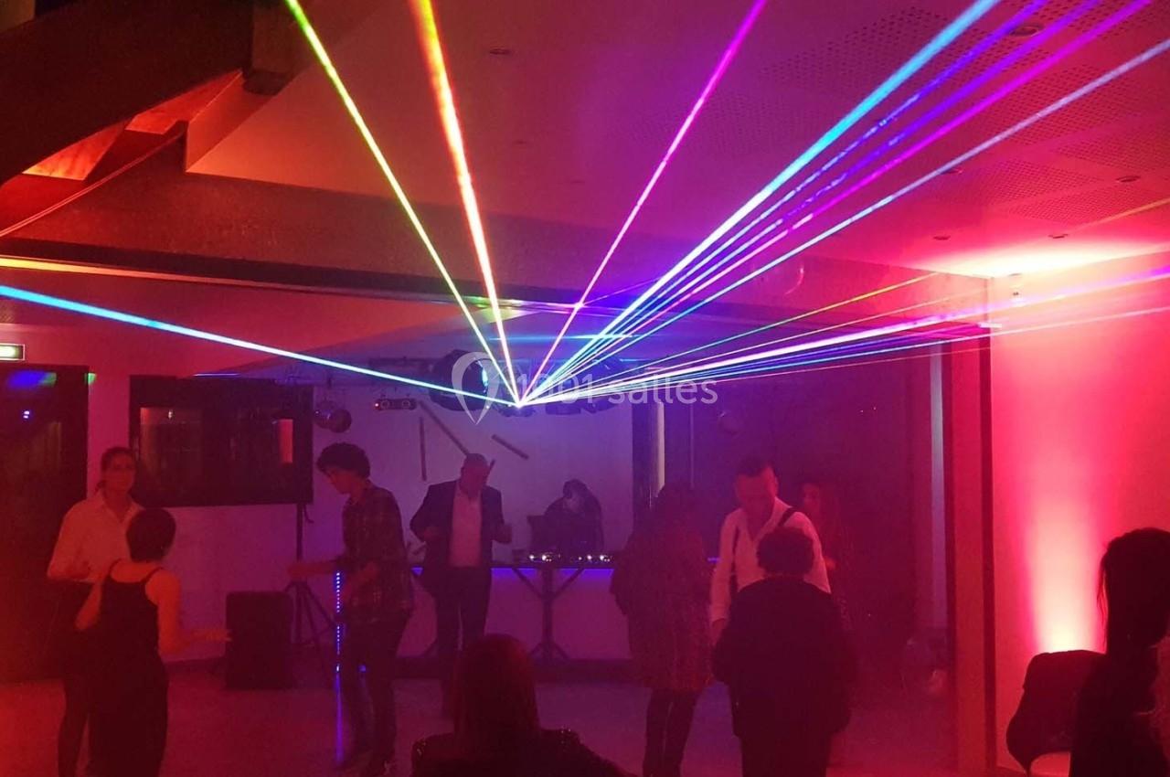 Des personnes dansent sous des faisceaux lumineux colorés dans une salle éclairée par des lumières tamisées.