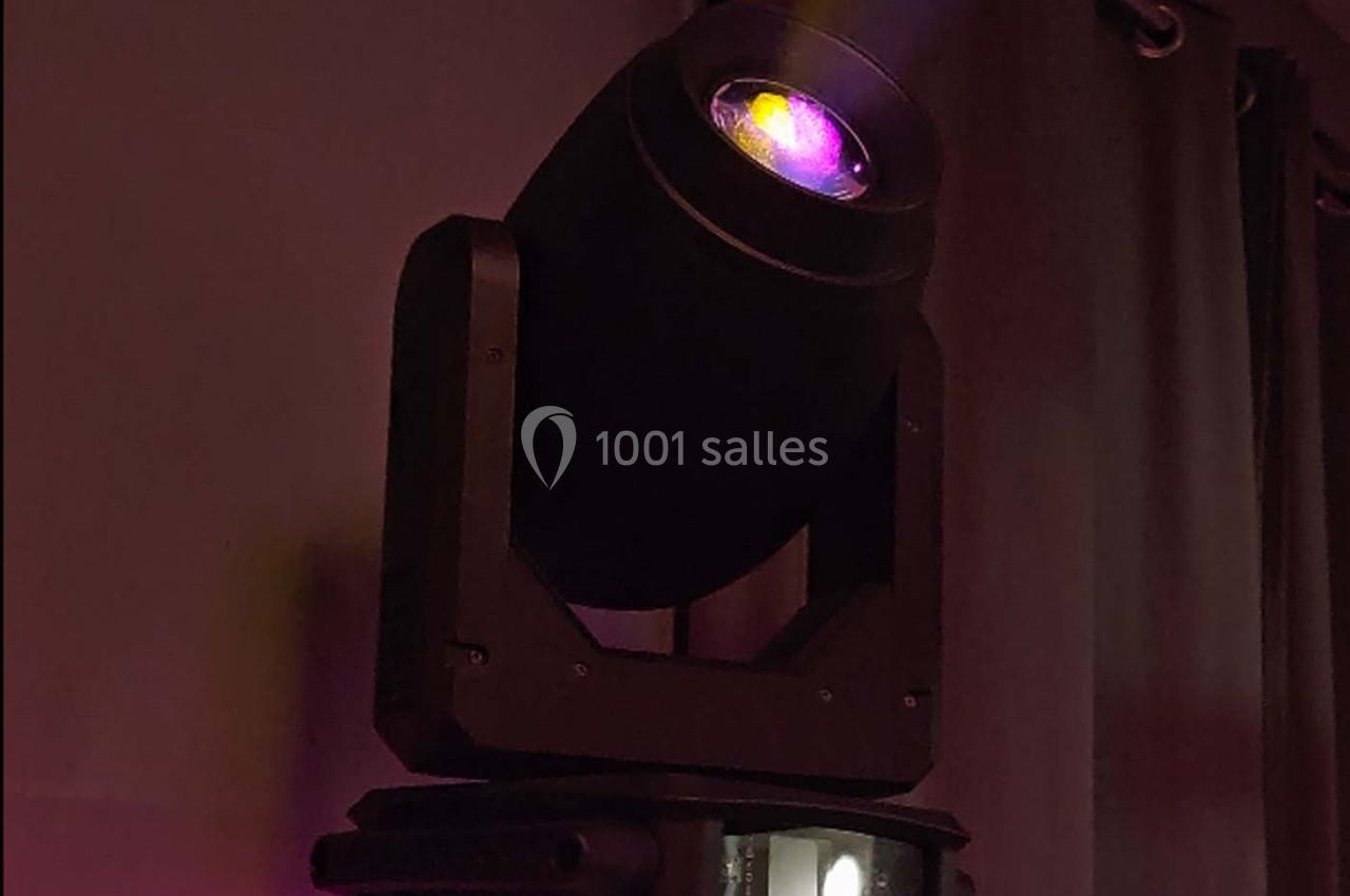 Projecteur de scène noir émettant une lumière violette dans un environnement sombre avec des rideaux en arrière-plan.