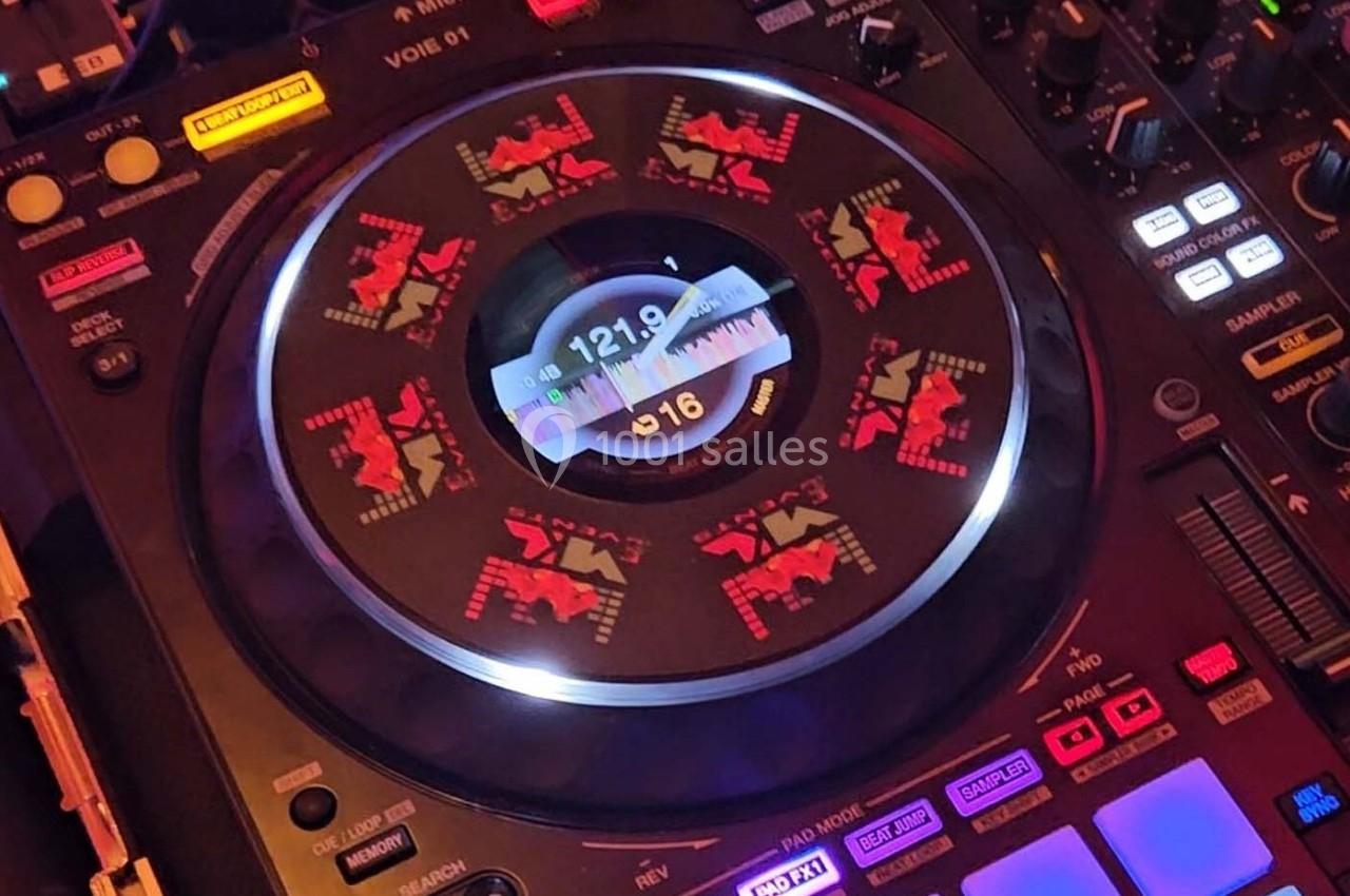 Platine DJ avec écran central affichant des informations sur la piste en cours, entourée de commandes lumineuses.