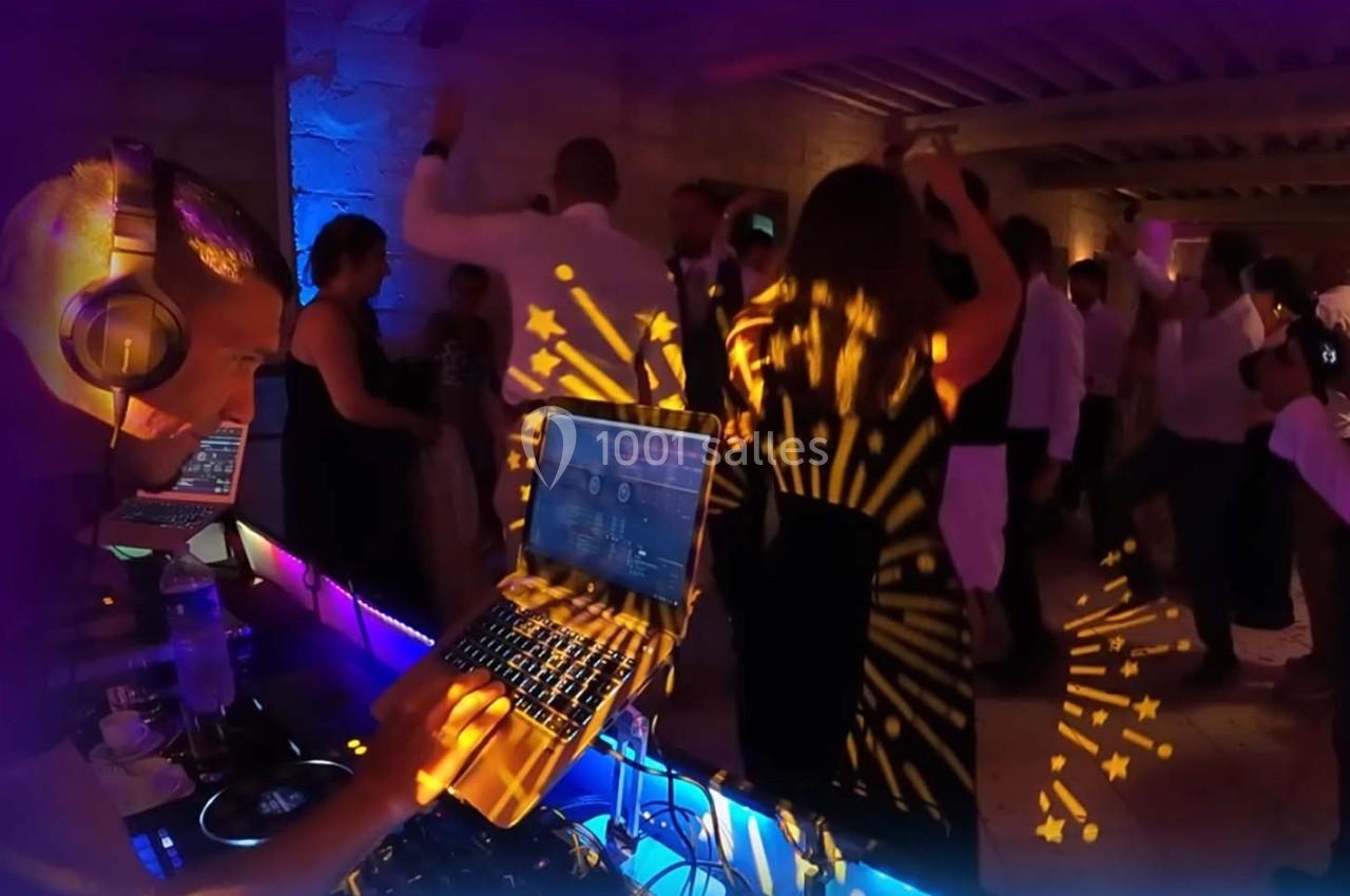 Un DJ mixe de la musique sur son ordinateur portable lors d'une soirée dansante avec des jeux de lumière colorés.
