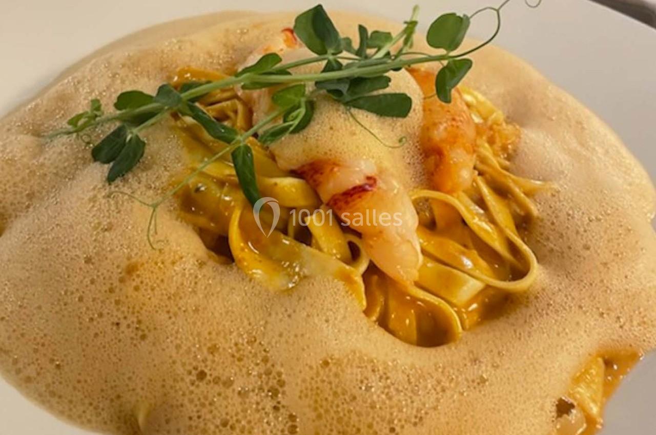 Assiette de pâtes aux crevettes, nappées d'une mousse légère et garnies de pousses de pois.