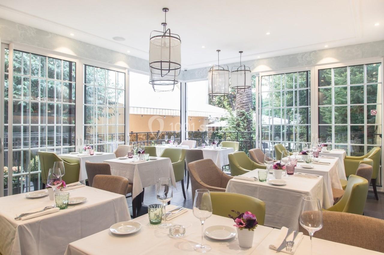 Salle de restaurant lumineuse avec grandes baies vitrées, tables dressées et chaises modernes dans un cadre élégant.