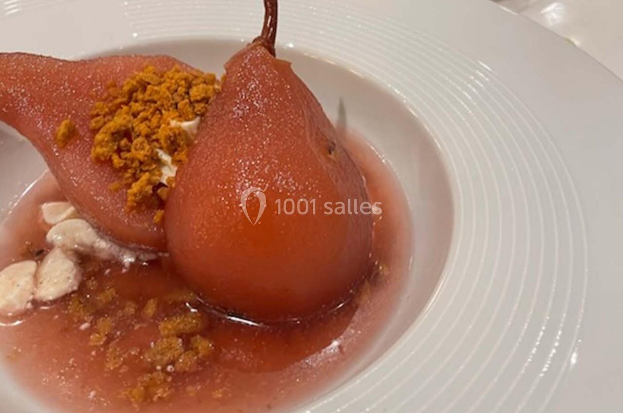 Poires pochées au sirop rouge servies avec une garniture croustillante et une sauce légère dans une assiette blanche.