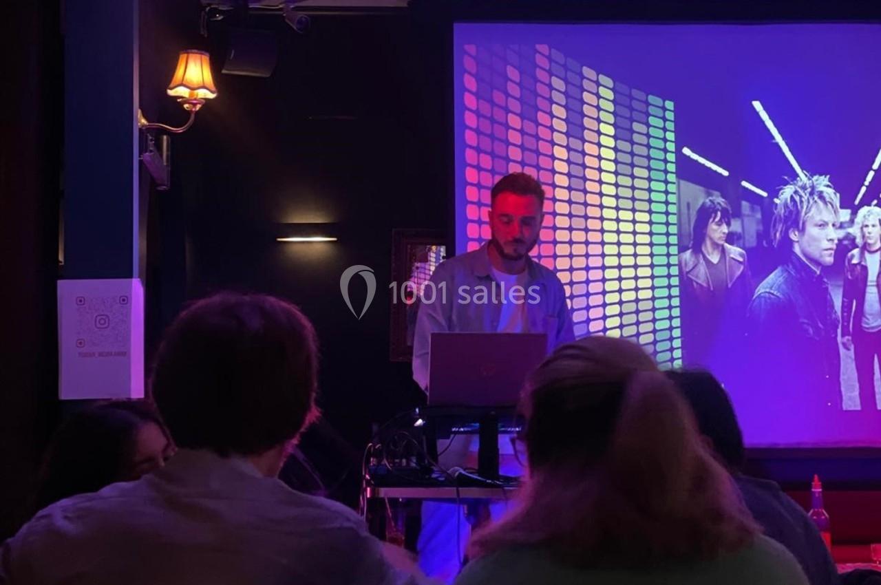 Un homme debout derrière un ordinateur, dans une salle sombre avec un écran projetant des images colorées.