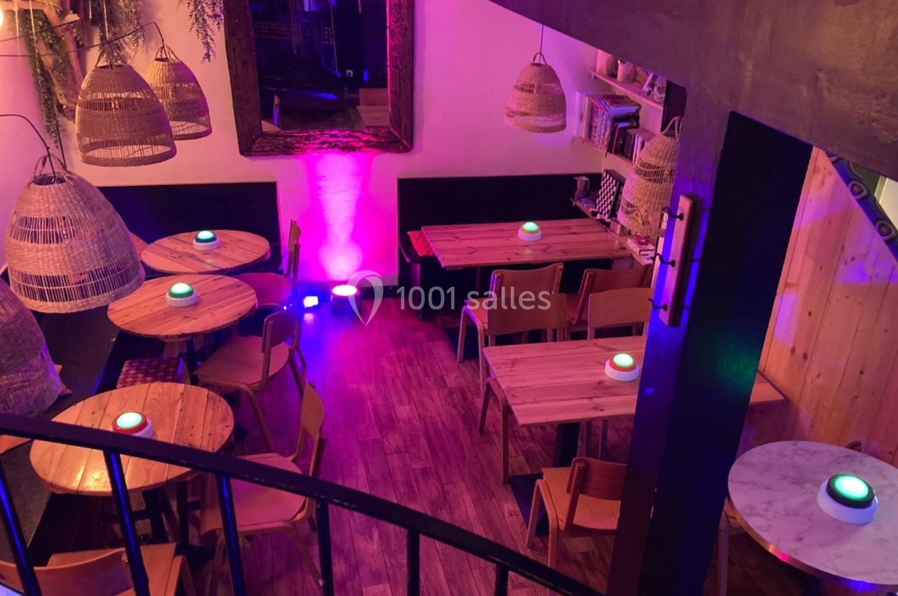 Salle de restaurant chaleureuse avec tables en bois, chaises simples et éclairage tamisé aux tons violets.