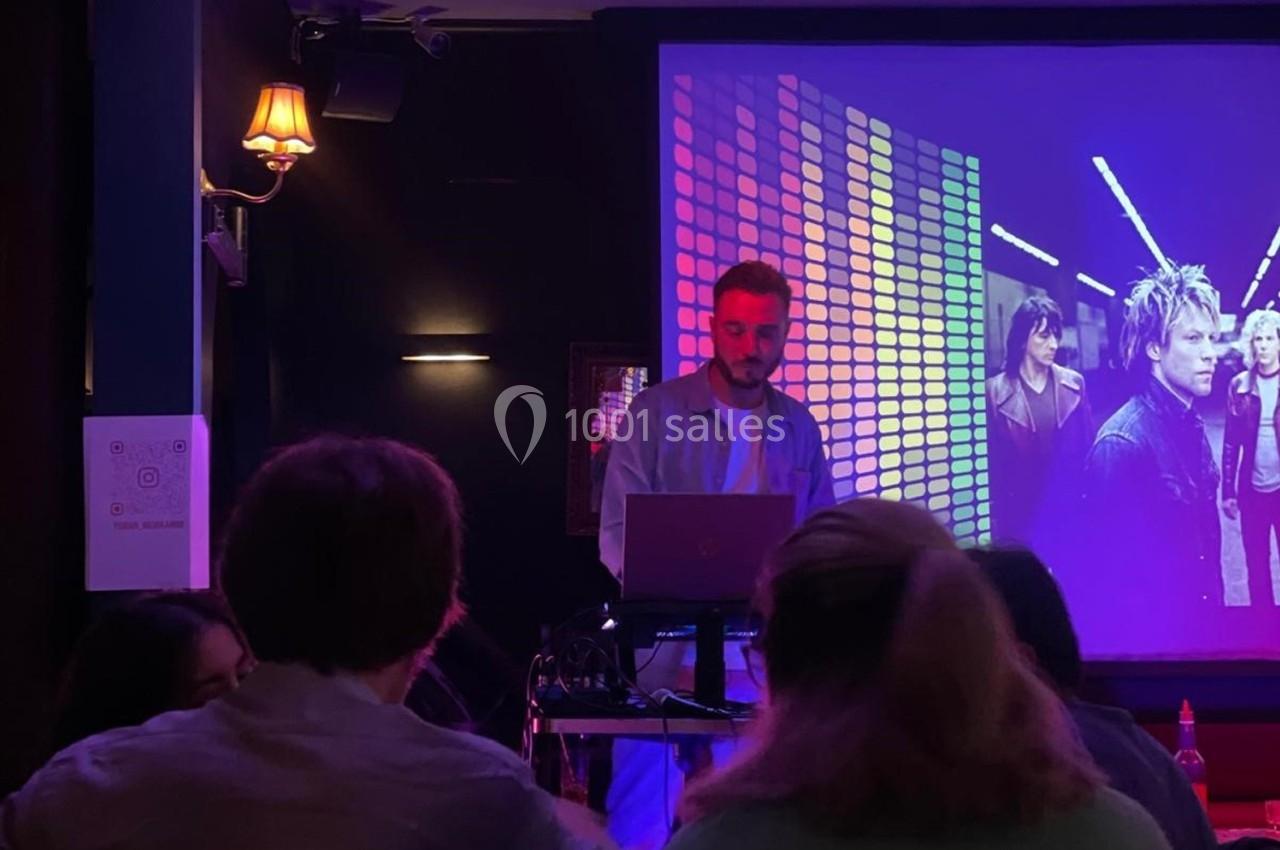 Un homme debout devant un ordinateur portable, projetant des images sur un écran dans une salle sombre.