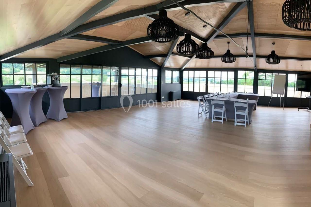 Salle lumineuse avec parquet clair, grandes baies vitrées, tables et chaises blanches, et décorations modernes.