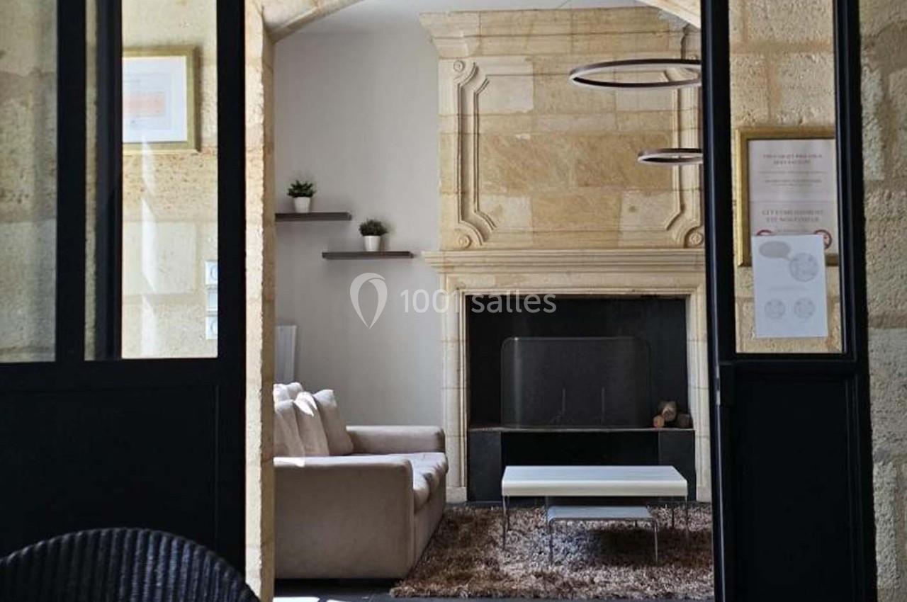 Salon avec cheminée en pierre, canapé beige, table basse blanche et étagères murales avec plantes.