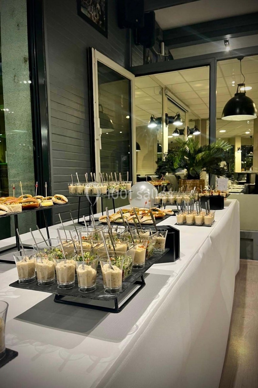 Buffet élégant avec verrines, amuse-bouches et petits sandwichs disposés sur une table blanche dans un cadre moderne.