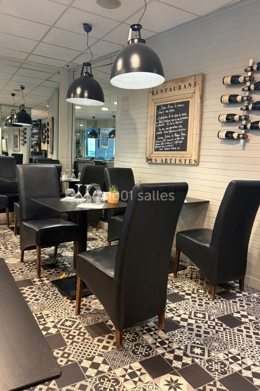 Salle de restaurant avec tables dressées, chaises noires, sol à motifs géométriques et ardoise murale affichant le menu.
